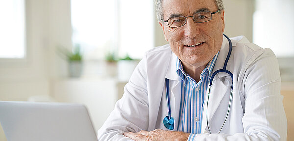 Arzt mit Brille und Stetoskop sitzt vor einem Notebook